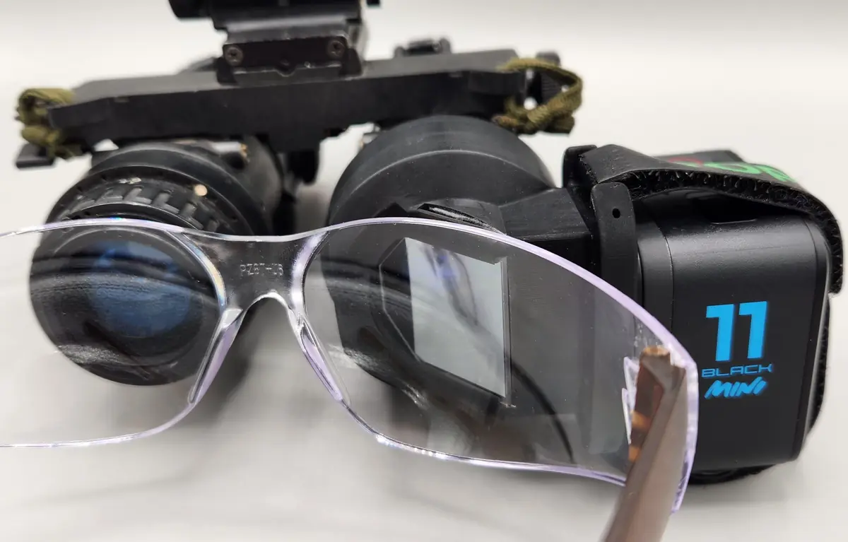 An NVGRA with a GoPro mounted on binocular night vision goggles, sitting just in front of clear eye protection